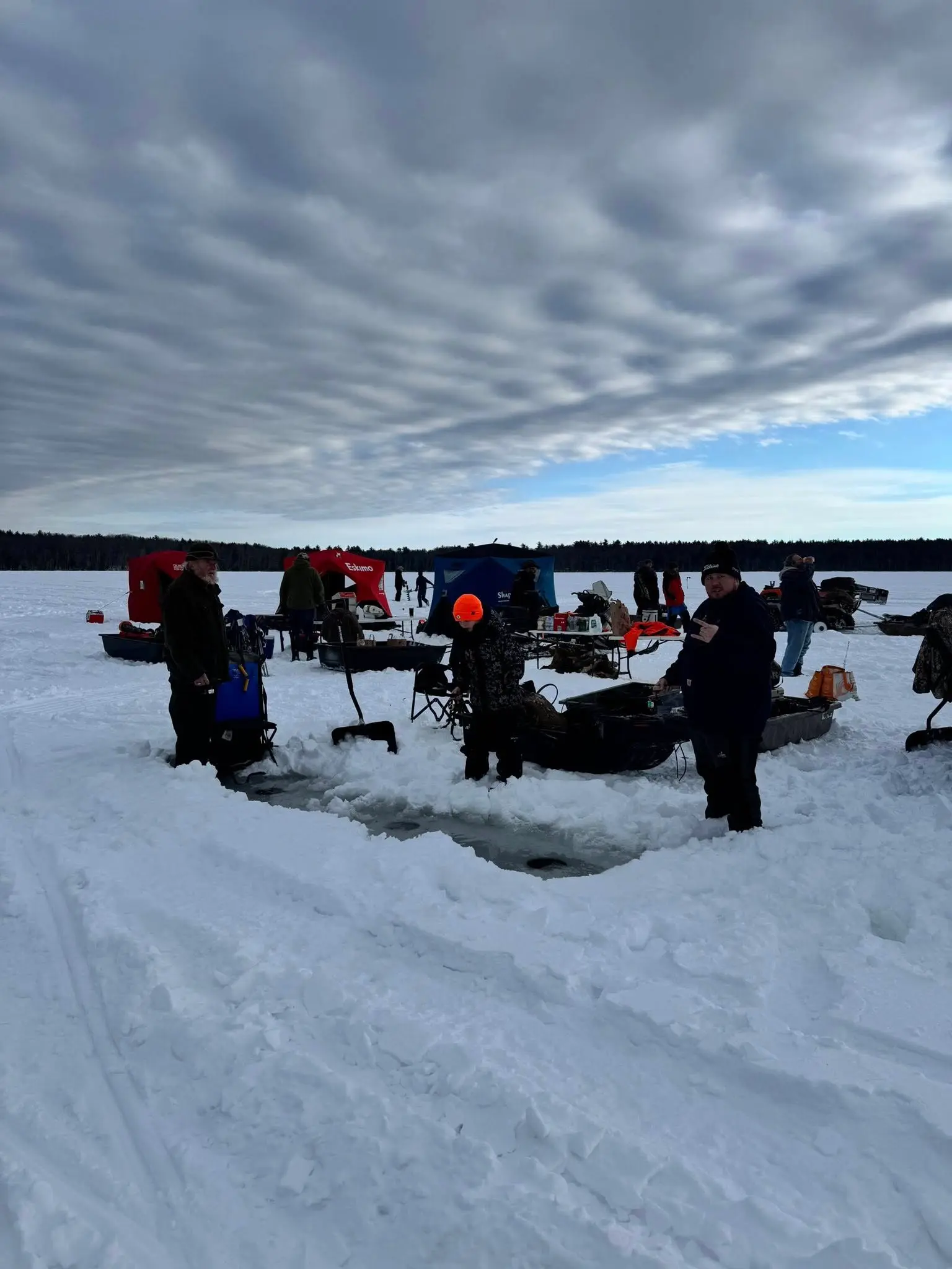 Wide view of the ice fishing setup with dramatic winter sky